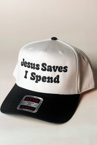 White and black cap with 'Jesus Saves I Spend' text on a beige background